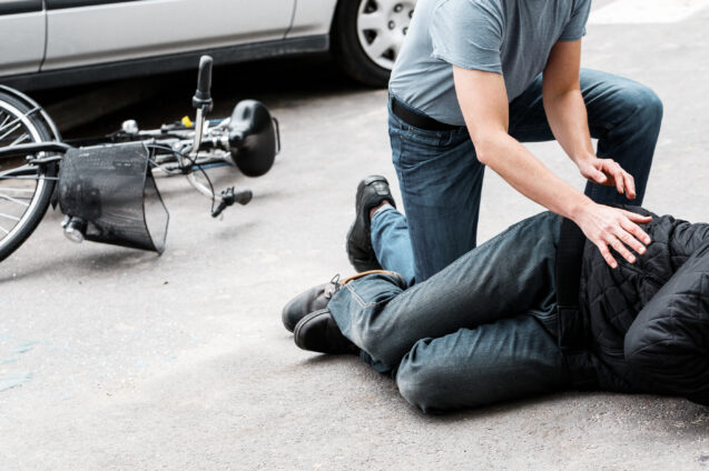 Pedestrian helping a victim of an automobile accident lying on the street next to a broken bike